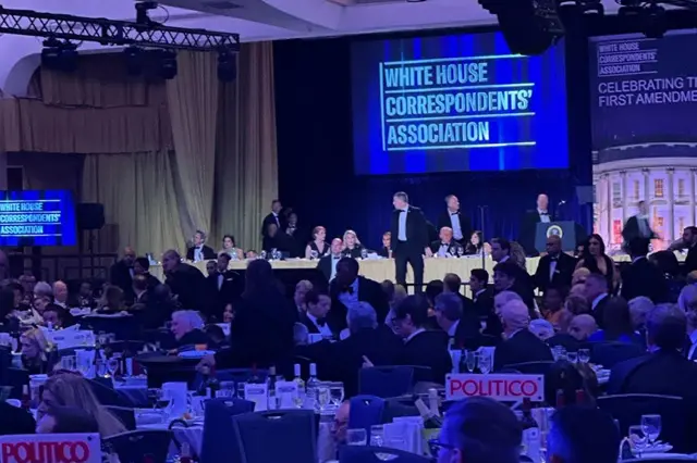 Attendees in formal attire ducking under tables during the chaotic shooting at the White House Correspondents' Dinner.