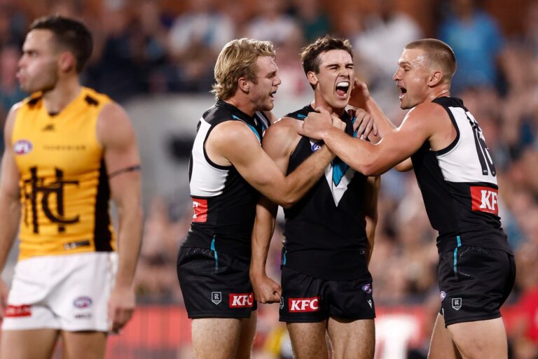 Hawthorn and Port Adelaide players fiercely contesting a center bounce during an AFL match at Marvel Stadium.