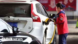 Petrol station attendant refueling a car as oil prices surge due to global tensions.