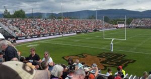 An aerial view of Kelowna's Apple Bowl stadium filled with a sold-out crowd during a Touchdown Kelowna CFL game, showcasing the vibrant atmosphere and economic impact.