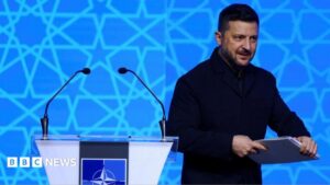 Ukrainian President Volodymyr Zelensky after addressing NATO, holding a binder of notes.