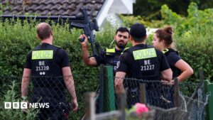 Image shows four police officers, one holding a gun up, at an allotment in Spandau, Berlin. This image depicts the police operation where the Berlin Pride attack suspect was killed.