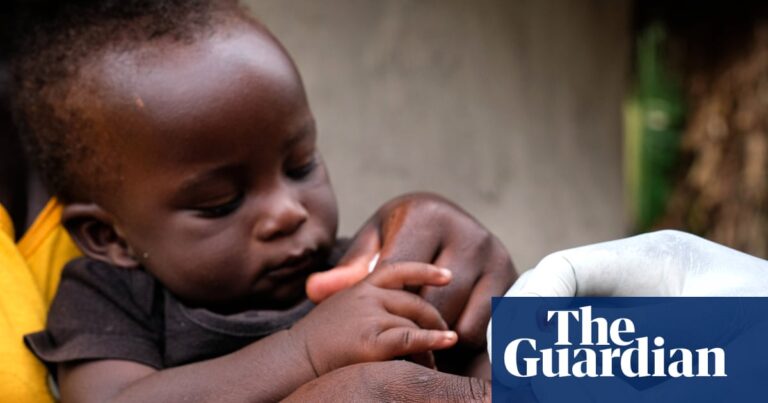 Close-up of a baby's hand being pricked for a blood sample by a health worker wearing white gloves in Uganda, part of a malaria program.