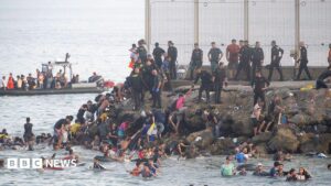 Image of thousands of migrants arriving in Ceuta, Spain's North African territory, showing crowded beaches and border areas.