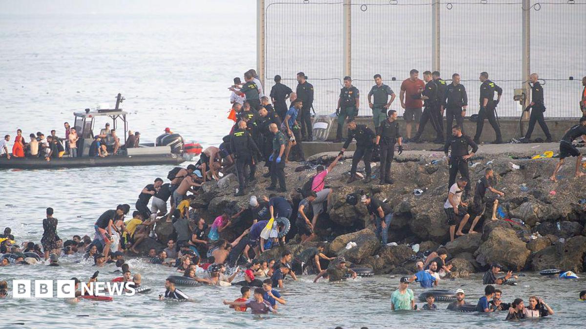 Image of thousands of migrants arriving in Ceuta, Spain's North African territory, showing crowded beaches and border areas.