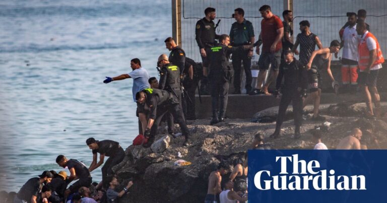 People climbing out of the sea onto a rocky shore in Ceuta