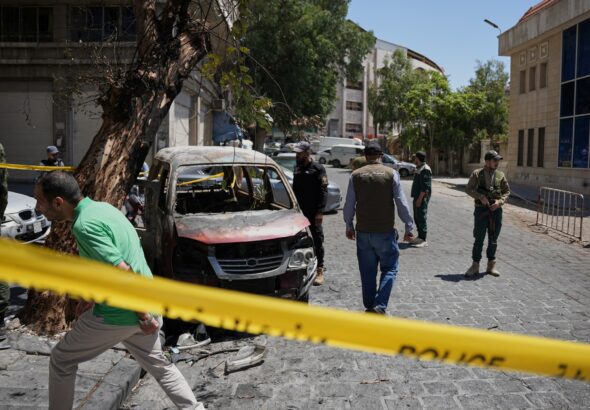 Security personnel inspect a burned vehicle in Damascus after two explosions rocked the area during French President Macron's visit.