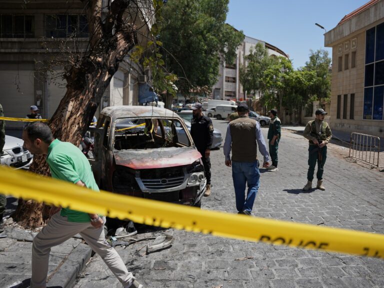 Security personnel inspect a burned vehicle in Damascus after two explosions rocked the area during French President Macron's visit.