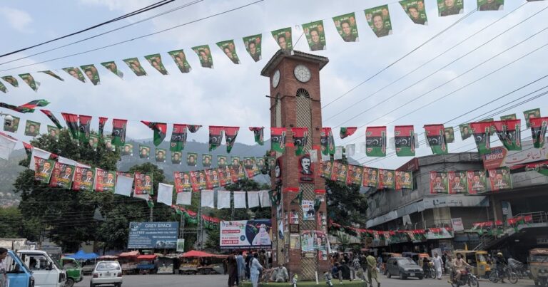 Election campaign posters are plastered across a government office compound in Muzaffarabad, Pakistan-administered Kashmir, depicting various political figures and party symbols.