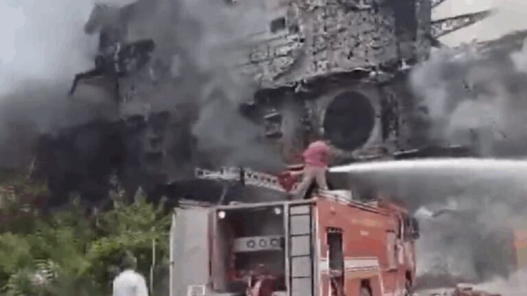 Image showing smoke billowing from the Kingdom of Dreams complex in Gurugram during a fire incident, with firefighters on the scene.