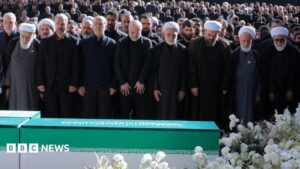 Image of thousands of mourners gathered at a funeral in Tehran, with senior Iranian officials in attendance, but Mojtaba Khamenei visibly absent.