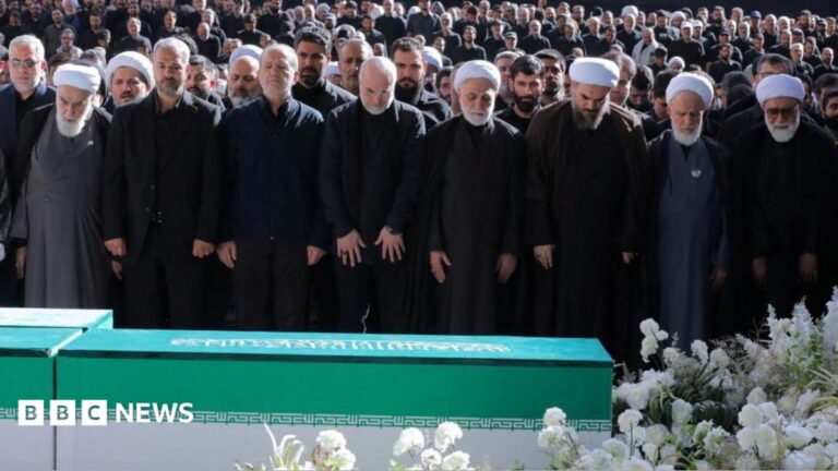 Image of thousands of mourners gathered at a funeral in Tehran, with senior Iranian officials in attendance, but Mojtaba Khamenei visibly absent.