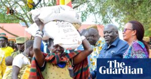 A Ugandan woman carrying grain on her head during food distribution, highlighting the crisis.