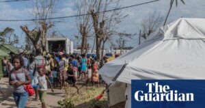 A shelter tent in Mozambique with 'UK aid' branding, surrounded by people and a distribution truck.