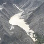 Image showing a barrier lake formed in a mountainous region near the Nepal-Tibet border, with an arrow indicating the direction of a flash flood.