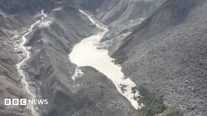 Image showing a barrier lake formed in a mountainous region near the Nepal-Tibet border, with an arrow indicating the direction of a flash flood.