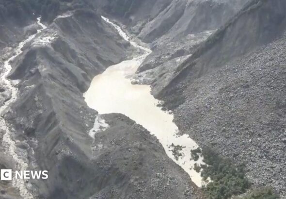Image showing a barrier lake formed in a mountainous region near the Nepal-Tibet border, with an arrow indicating the direction of a flash flood.