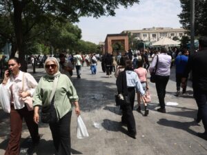 An Iranian man walks through the Grand Bazaar in Tehran, with blurry figures in the background. The atmosphere appears subdued.
