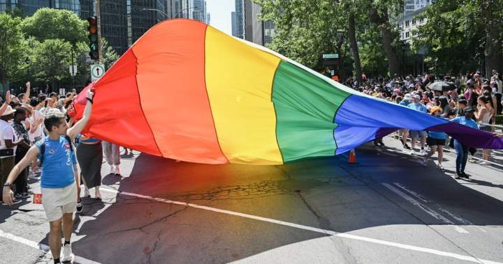 A large rainbow flag being carried by participants during the Montréal Pride Parade