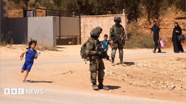 Image of Palestinian families walking on a dusty road with Israeli soldiers in the background, amidst reported displacements in Qusra, West Bank.