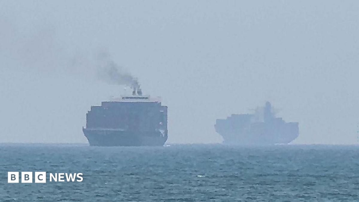 Cargo ships anchored near the Strait of Hormuz, emphasizing regional tensions and shipping routes.