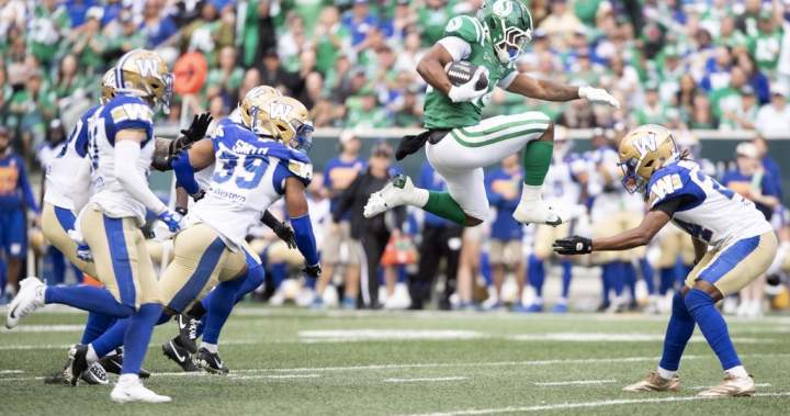 Roughriders running back Quali Conley (24) leaps over Winnipeg Blue Bombers defenders during CFL action.