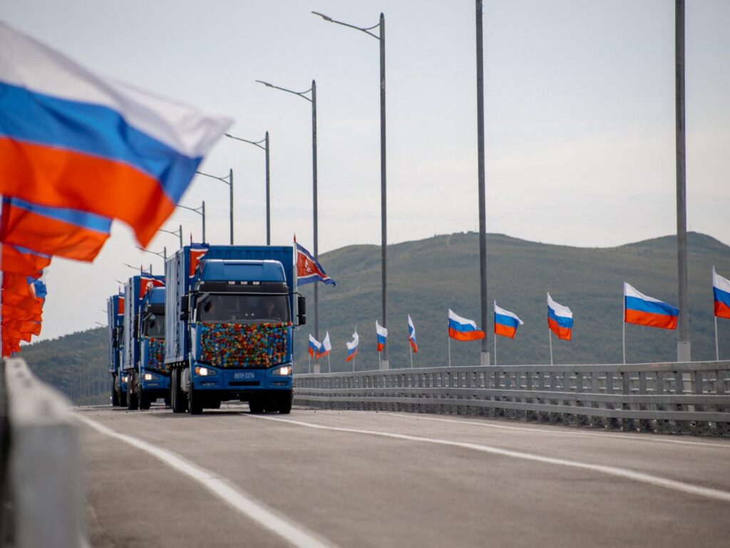 New Russia-North Korea road bridge over the Tumen River with national flags waving and trucks crossing.