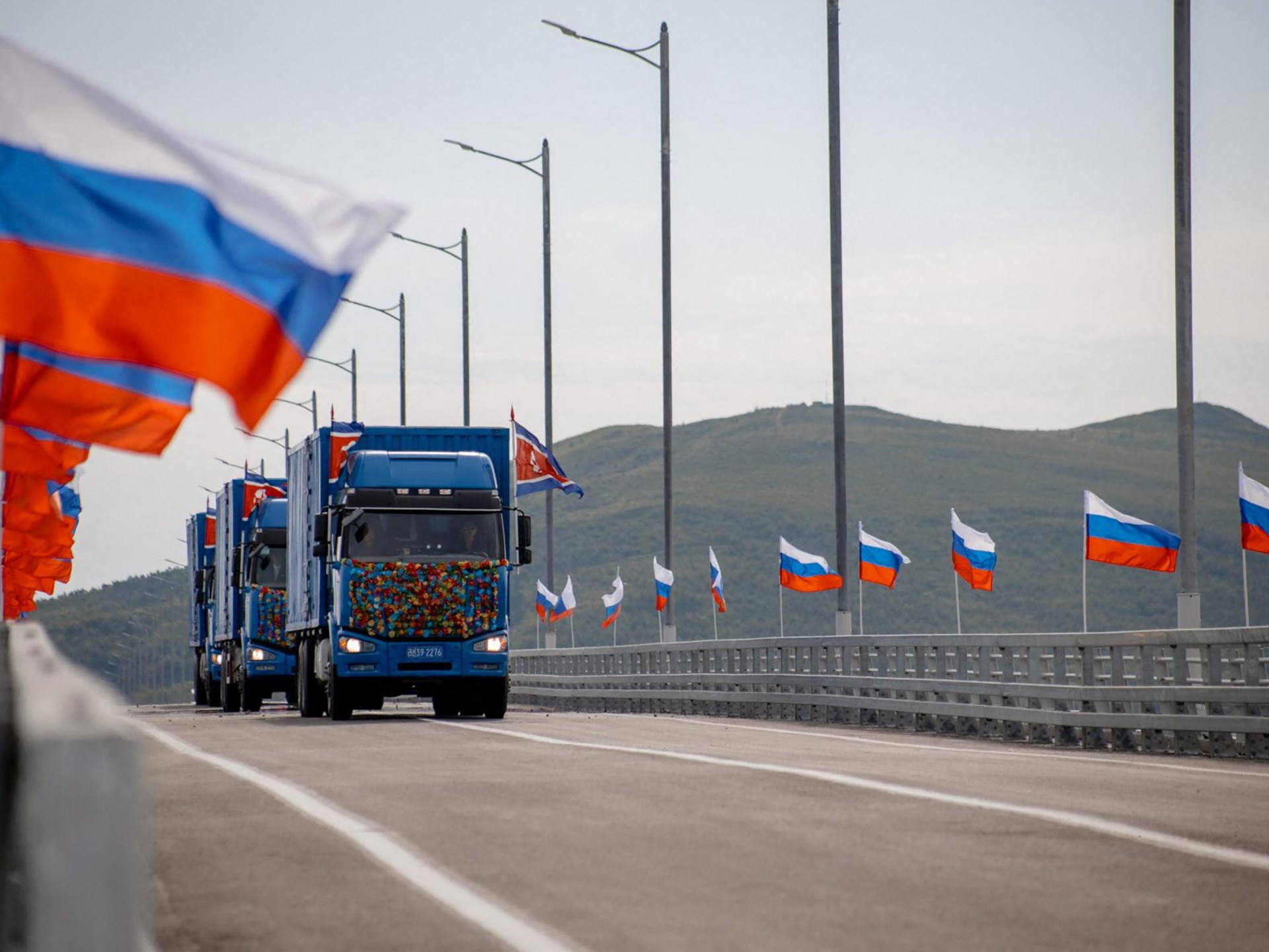 New Russia-North Korea road bridge over the Tumen River with national flags waving and trucks crossing.