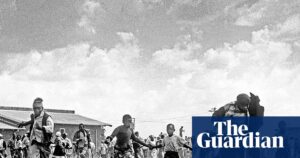 Black and white image of adults and children running in panic through grass with buildings in the background during the Sharpeville Massacre.