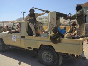 Yemeni government soldiers on a pickup truck in Mukalla, against a backdrop of conflict.