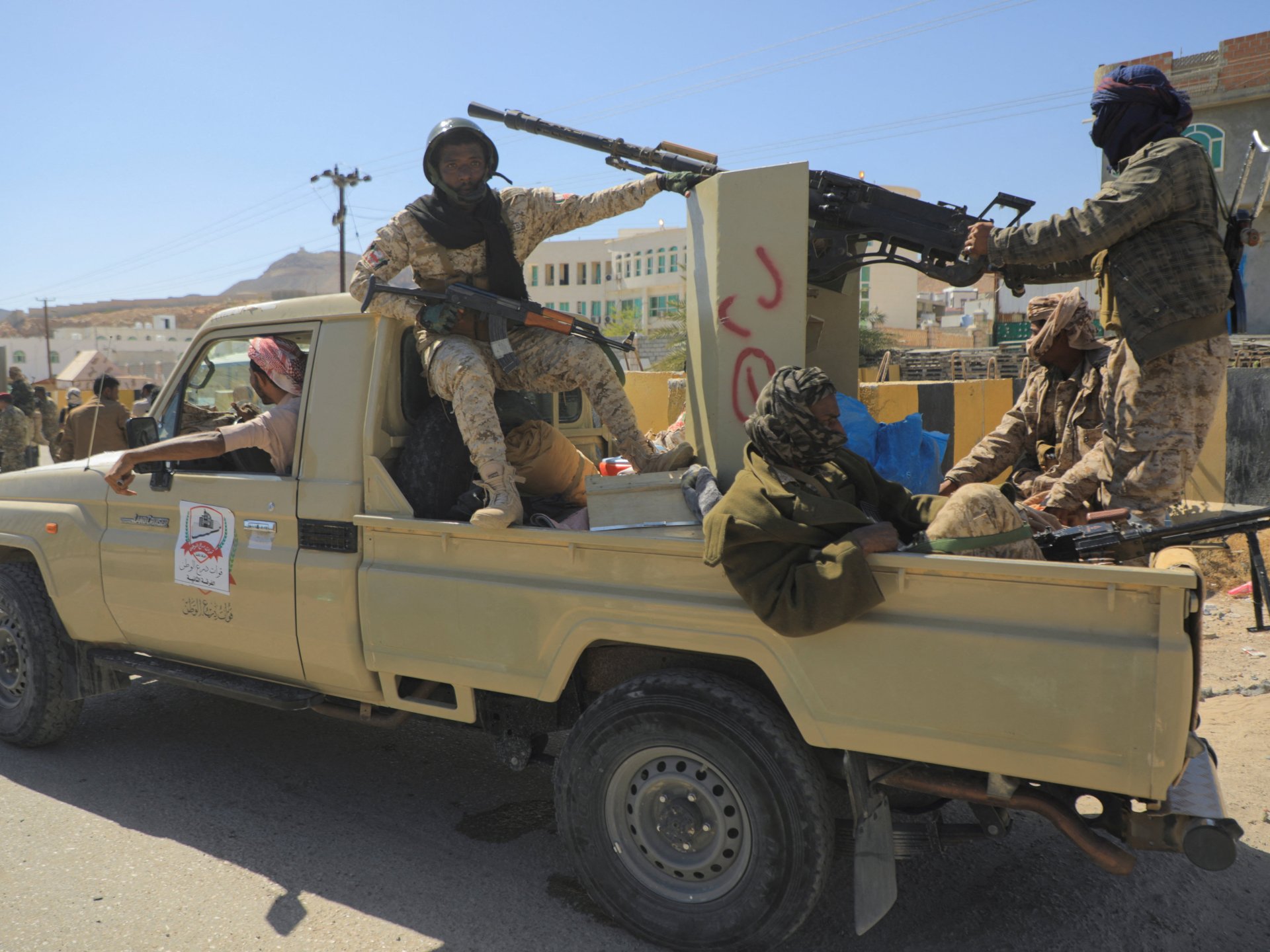 Yemeni government soldiers on a pickup truck in Mukalla, against a backdrop of conflict.